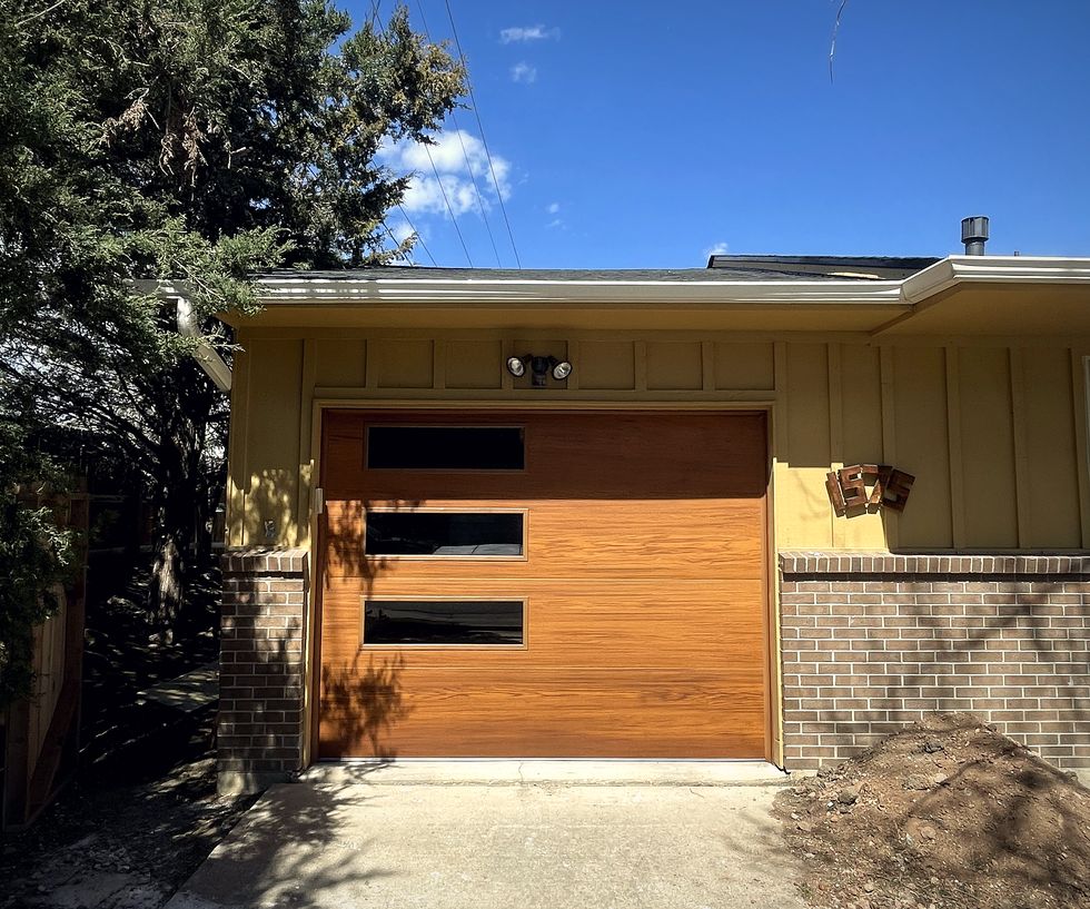 A modern flush wood garage door on a mid century house, tree shadows across the drive