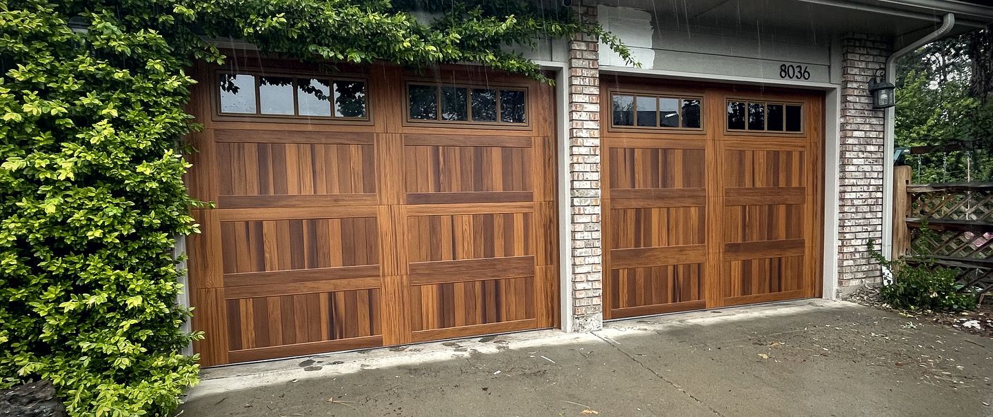 Two mahogany garage doors on a brick house with climbing vines across the header