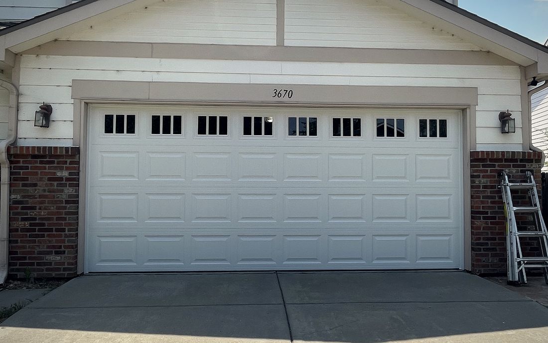 A white garage door with a window row on a brick and siding two storey house