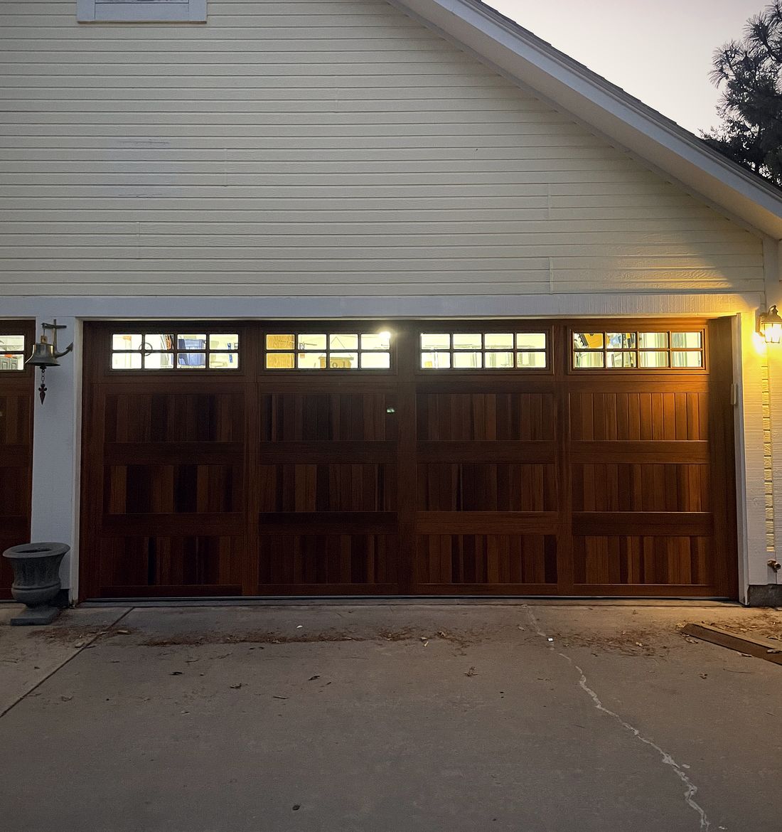 A wide mahogany carriage house garage door at dusk, warm light showing through the top window row