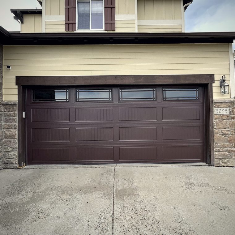 A dark brown raised panel garage door with a window row on a two storey house