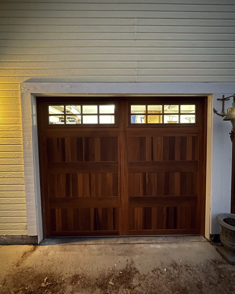 A mahogany carriage house door with a window row, on a pale sided house
