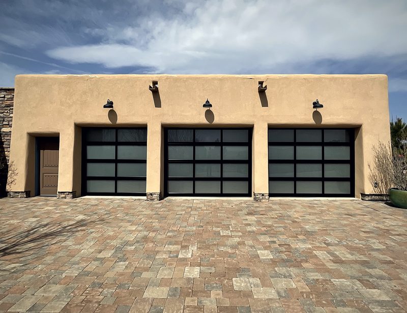 Three full view aluminium and glass garage doors on an adobe house with a paver drive