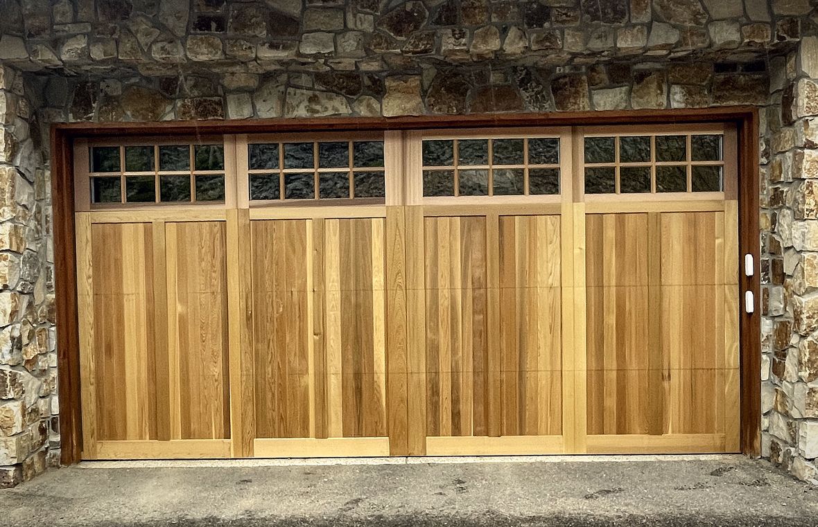 A light cedar carriage house door with window lights, set in a stone faced house