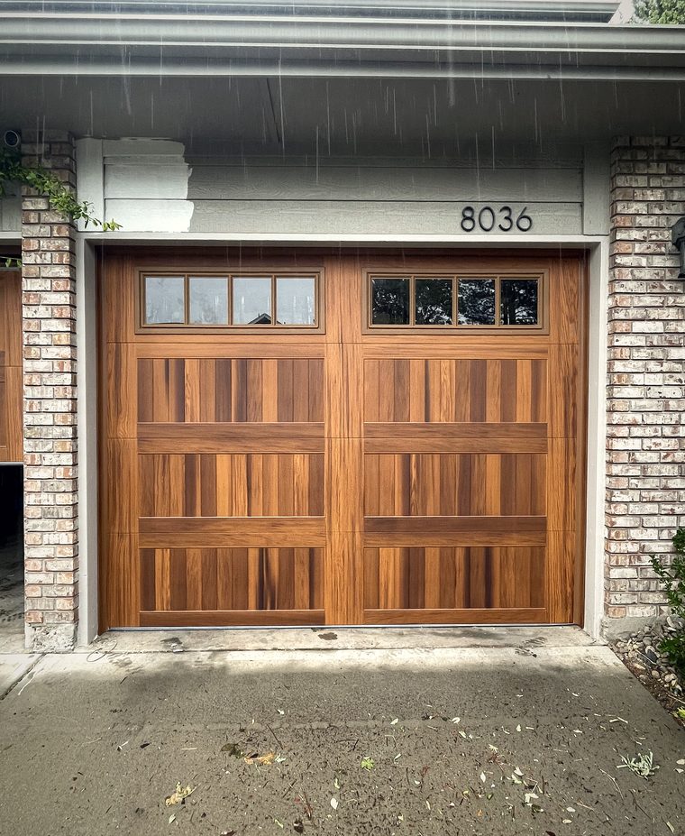 A mahogany garage door with window lights, brick surround, in the rain