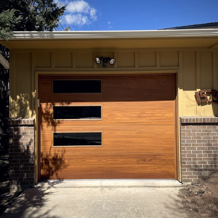 A modern flush wood garage door with three offset black window slots