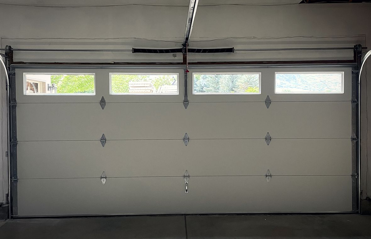 A garage door opener and rail above a wide pale sectional door, seen from inside