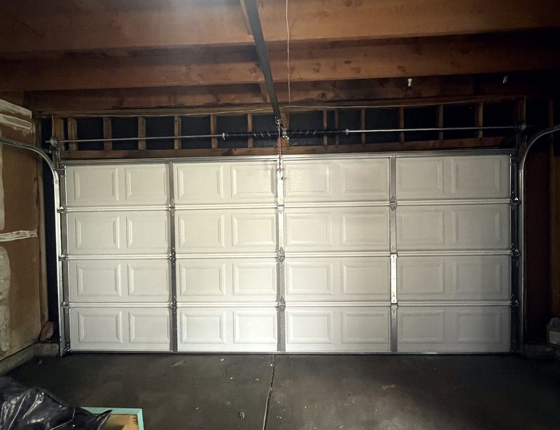 A new pale sectional door fitted inside a garage with an exposed timber ceiling