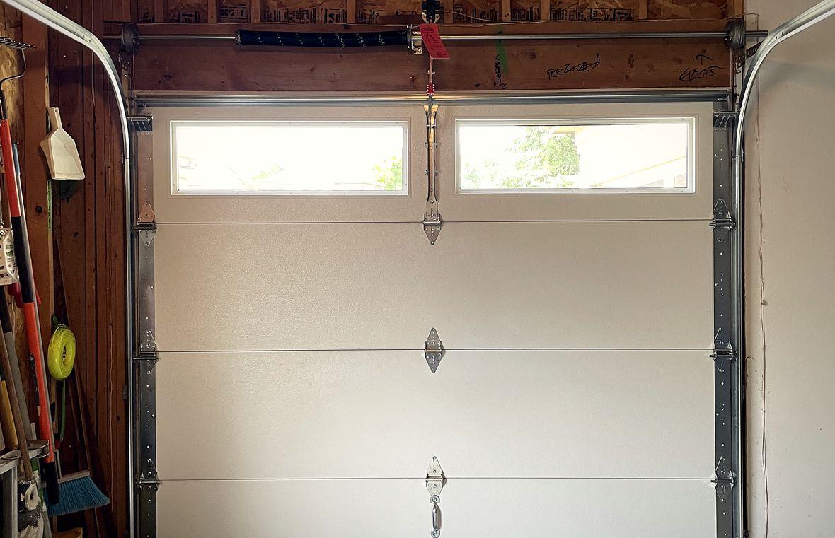 Inside a garage with tools on the wall and a single pale sectional door closed in its frame