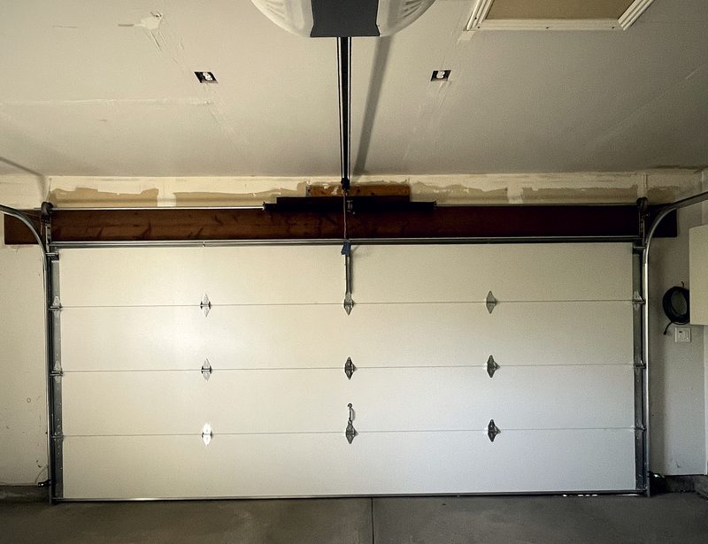 A ceiling mounted garage door opener above a closed pale door