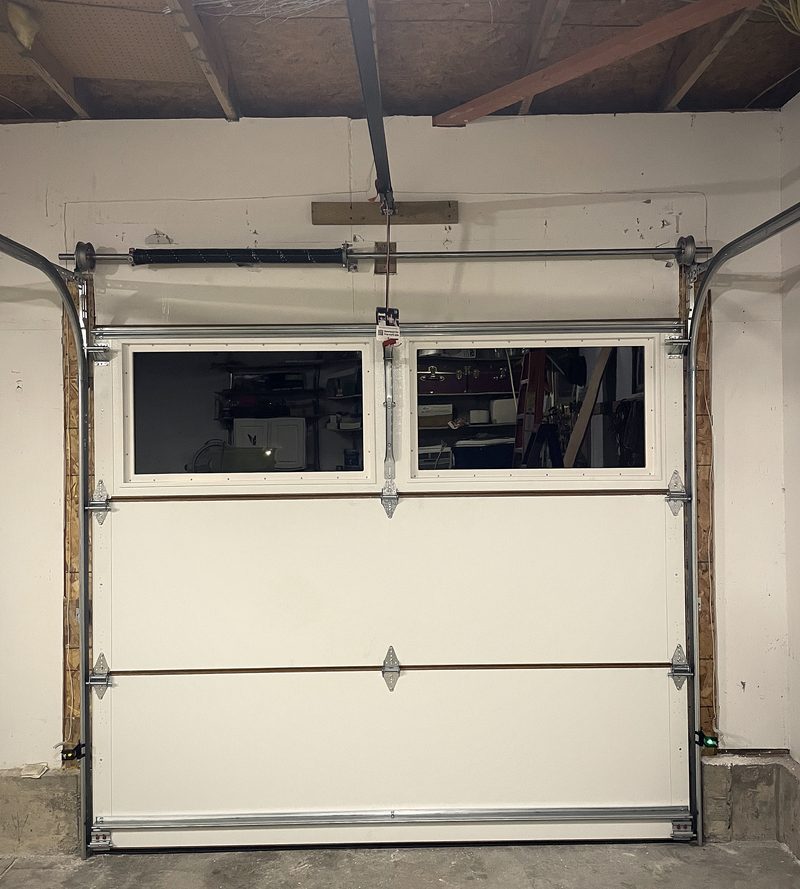 A garage door and its track hardware seen from inside, framing exposed overhead