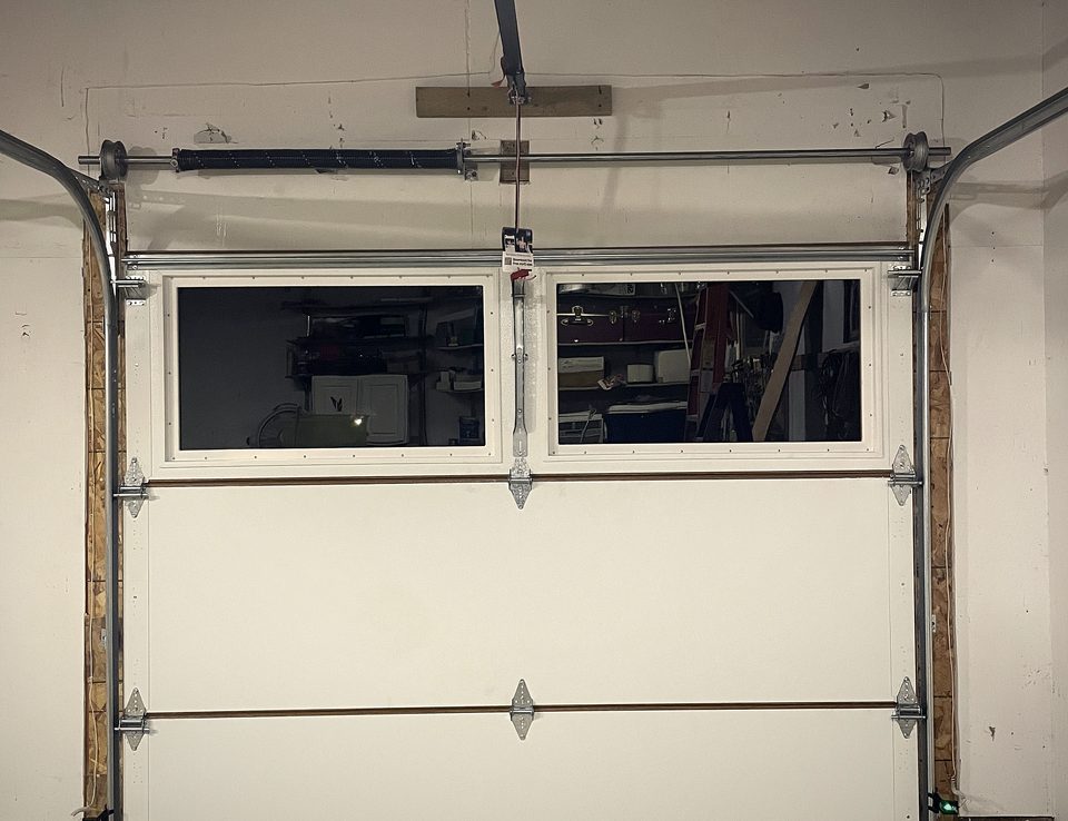 A garage door sitting in its track from inside, with the opener rail and spring shaft above it