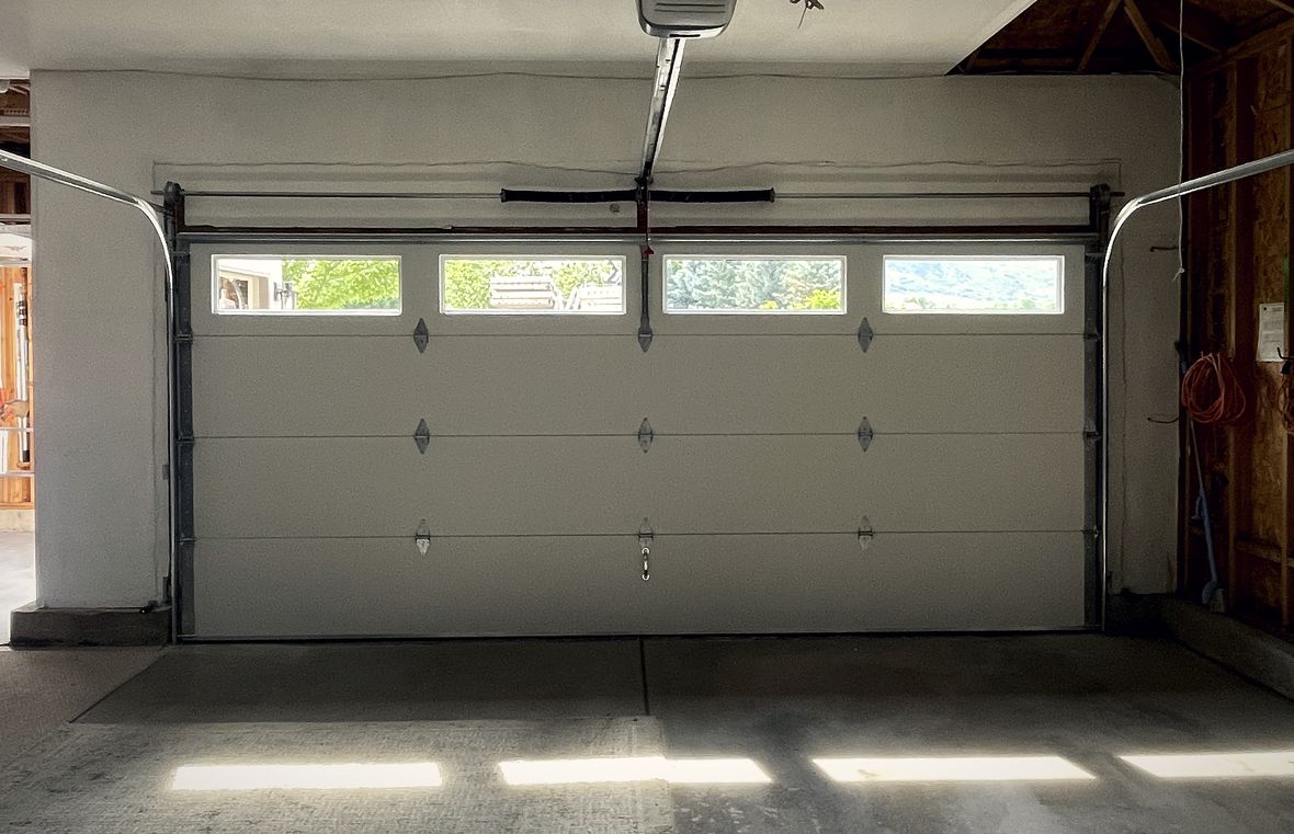 A wide pale sectional garage door from inside, sunlight striping the floor