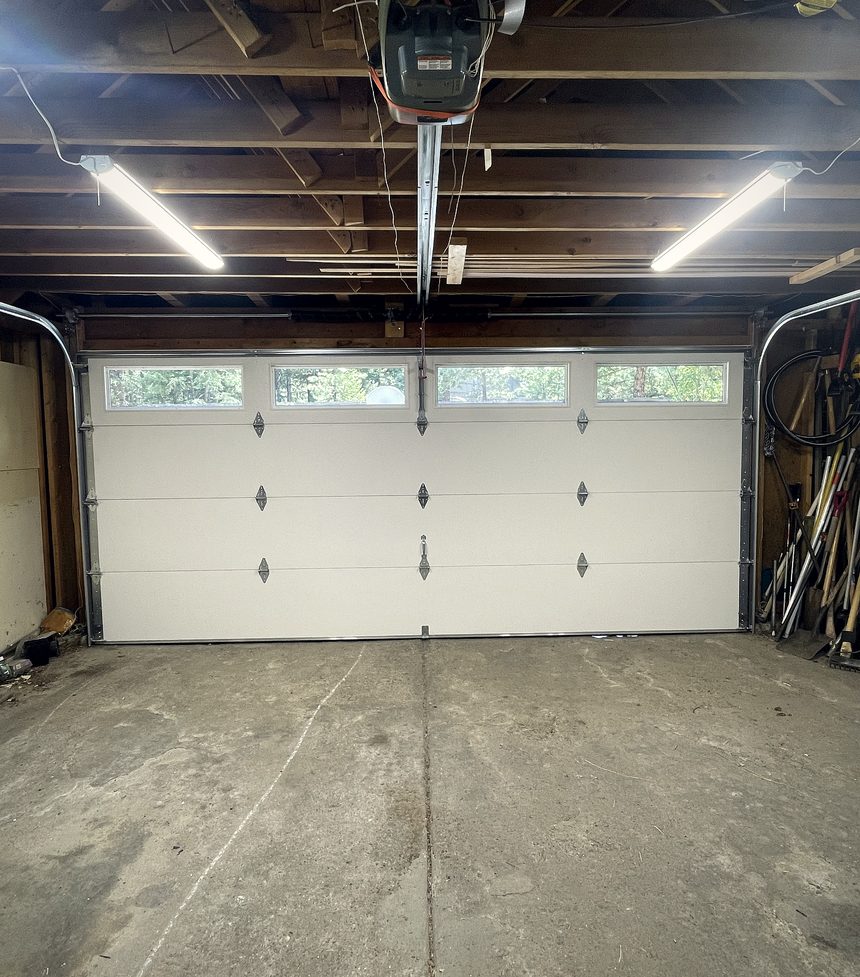 A tidy garage lit from above, a pale sectional door closed across the opening