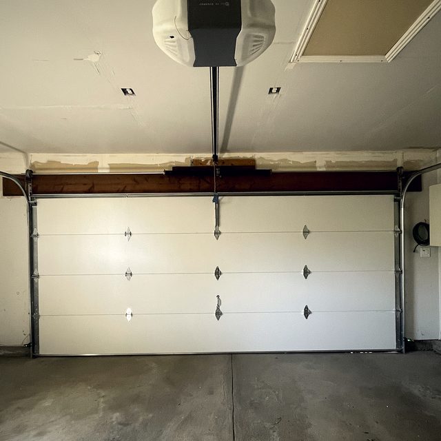 A garage door opener head mounted to the ceiling above a closed door