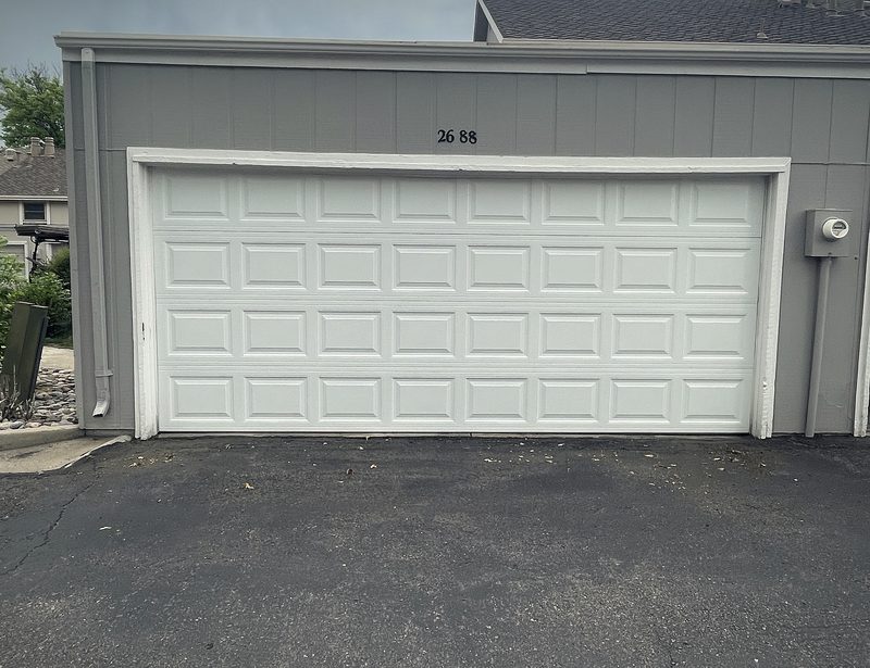 A white long panel garage door on a grey sided house