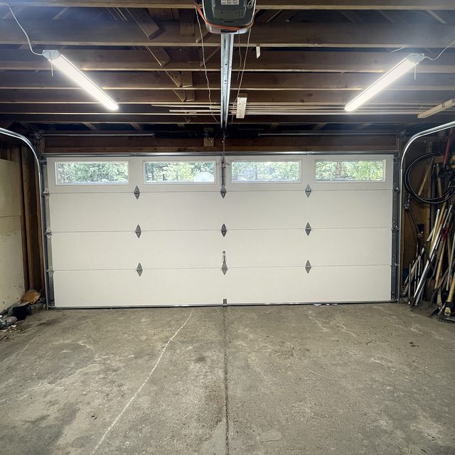 A pale sectional garage door closed across a lit garage