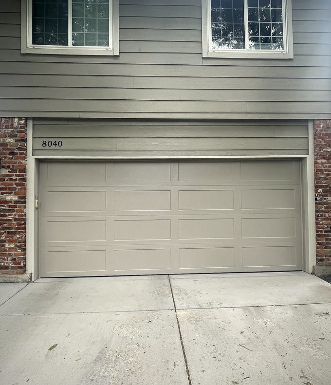 An almond raised panel garage door on a grey sided house