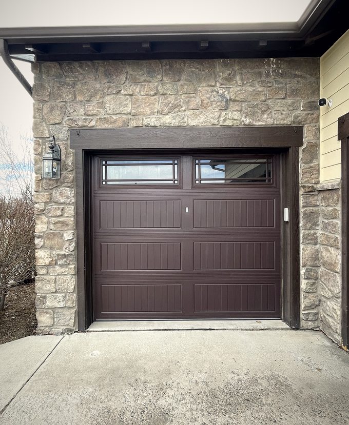 A dark brown garage door with a window row in a stone faced opening