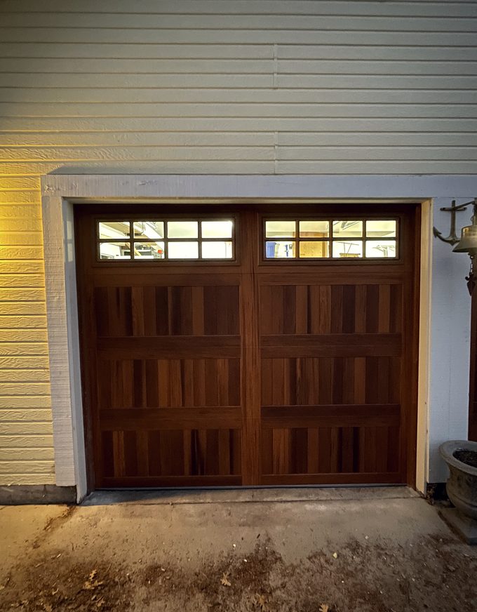 A mahogany carriage house door with a window row on a pale sided house