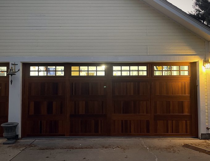A mahogany carriage house garage door lit from inside at dusk