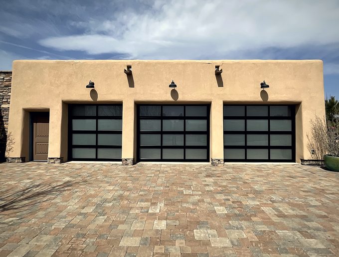 Three full view glass garage doors on an adobe house