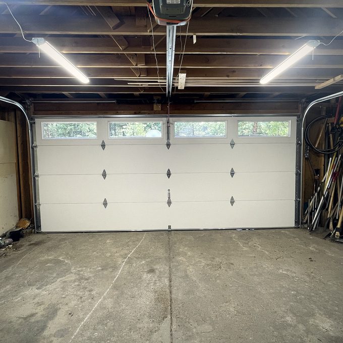 A pale sectional garage door closed across a lit garage