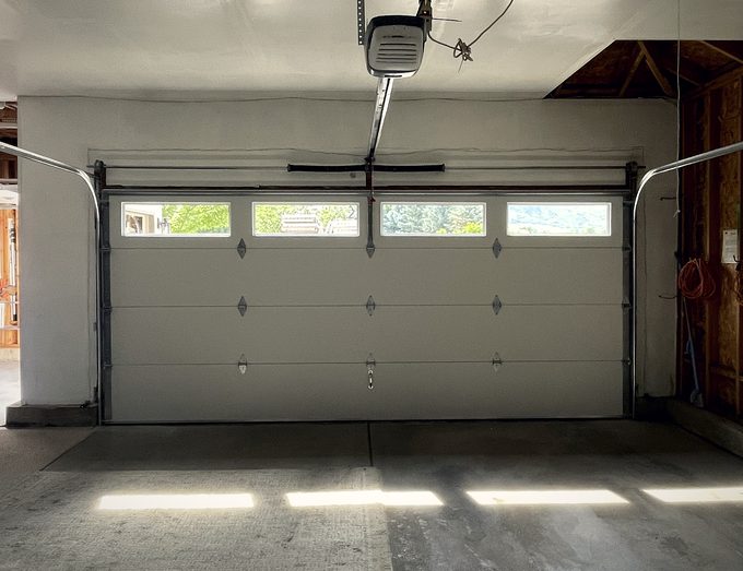 A wide pale garage door from inside with sun striping the floor