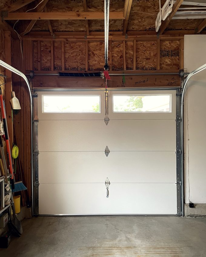 A single bay garage door with tools hanging on the wall beside it