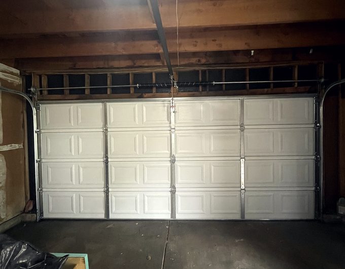 A newly fitted pale garage door inside a garage with a timber ceiling