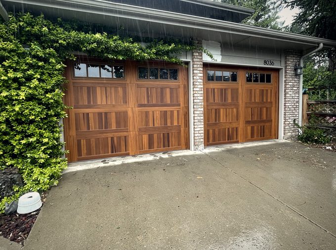 Two mahogany garage doors on a brick house under climbing vines