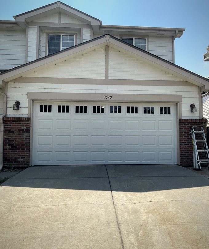 A white garage door with a window row, ladder standing to one side